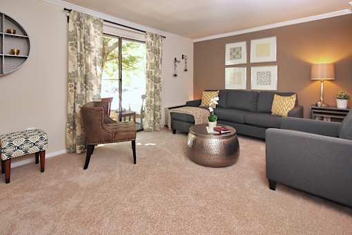 A living room with a grey couch, a brown chair, a round coffee table, and a small potted plant on a side table.