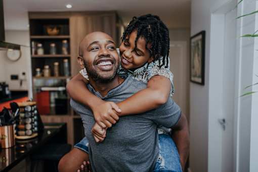 A man is giving a piggyback ride to a young girl in a kitchen.