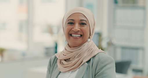 A woman wearing a light-colored hijab smiles at the camera.