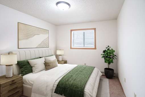 A bedroom with a bed, nightstand, and a plant. Fargo, ND Cedars 4 Apartments