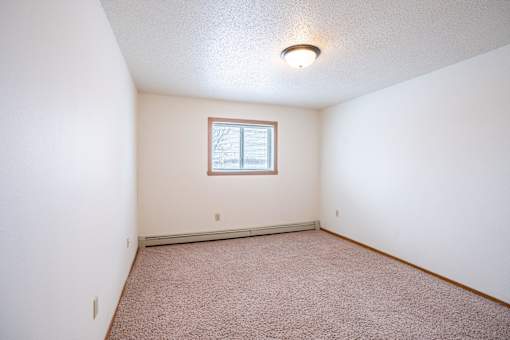 A room with a window and carpeted floor. Fargo, ND Cedars 4 Apartments