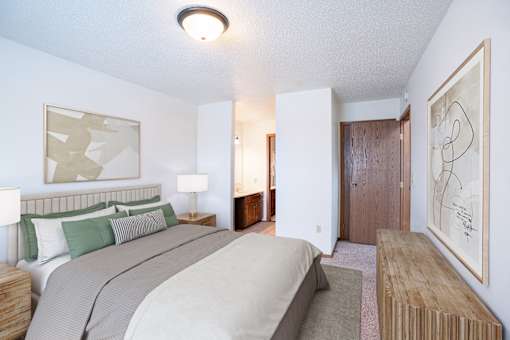 A bedroom with a bed, nightstand, and artwork on the wall. Fargo, ND Cedars 4 Apartments