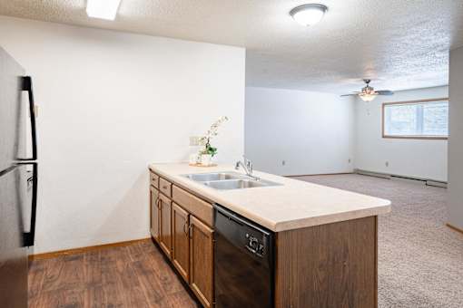 A kitchen with a sink, refrigerator, and wooden cabinets. Fargo, ND Cedars 4 Apartments