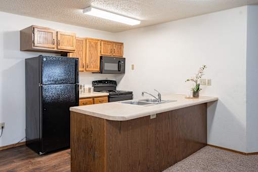 A kitchen with a black fridge, microwave, and wooden cabinets. Fargo, ND Cedars 4 Apartments