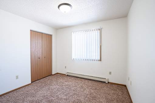 A room with a brown carpet and a window with blinds.