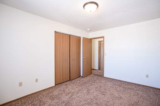 A room with a carpeted floor and a white wall with a brown door and a brown wardrobe.