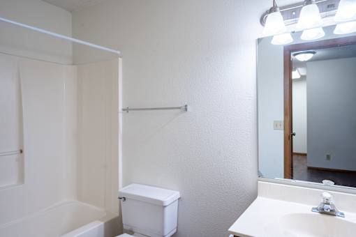 A white bathroom with a toilet, sink, and mirror. Fargo, ND Candlelight Apartments