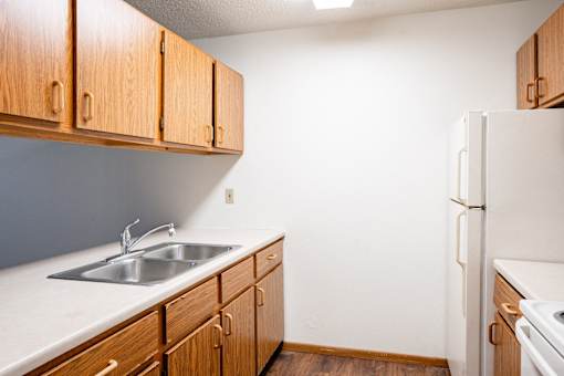 A kitchen with wooden cabinets and a white refrigerator. Fargo, ND Candlelight Apartments