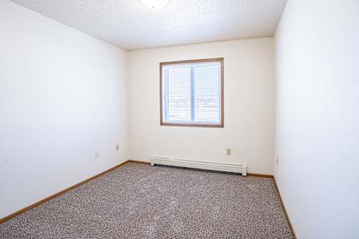 A room with a window and a carpeted floor. Fargo, ND Country Edge Apartments