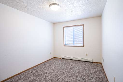 A room with a window and a carpeted floor. Fargo, ND Country Edge Apartments