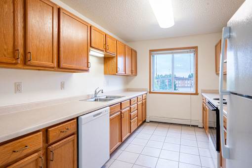 A kitchen with wooden cabinets and a white dishwasher. Fargo, ND Summit Point Apartments