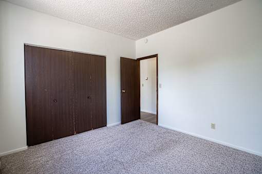 A room with a carpeted floor and two doors. Bismarck, ND Belmont Apartments