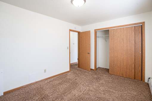 A room with a brown carpet and two wooden doors. Fargo, ND Birchwood 2 Apartments