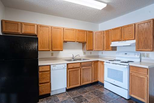 A kitchen with wooden cabinets and black appliances. Dilworth, MN Fieldstone Apartments