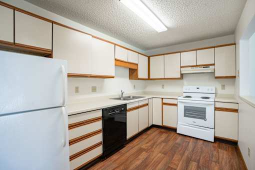 A white refrigerator is in a kitchen with wooden floors and white cabinets.