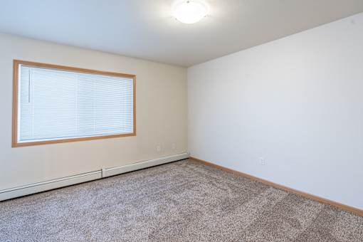 A room with a carpeted floor and a window with blinds. Moorhead, MN Sandy Creek Apartments