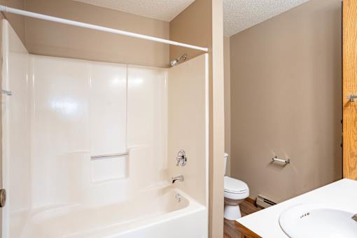 A white bathtub with a shower head and a white sink with a brown cabinet.