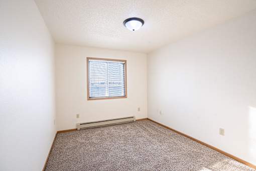 A room with a window and carpeted floor. Fargo, ND Fieldstone Apartments