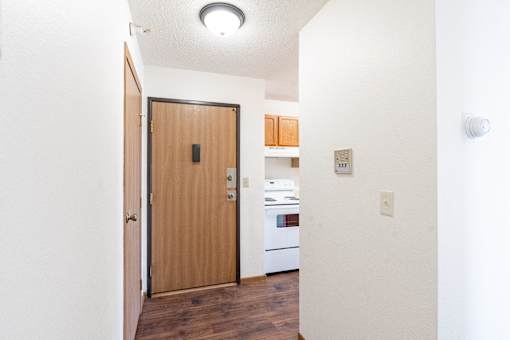 A white hallway with a brown door leading to a kitchen. Fargo, ND Fieldstone Apartments