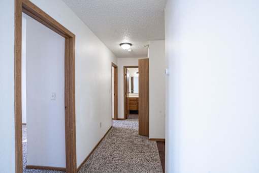 A long hallway with a carpeted floor and white walls. Fargo, ND Fieldstone Apartments