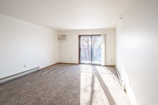 A room with a carpeted floor and a sliding glass door leading outside. Fargo, ND Fieldstone Apartments