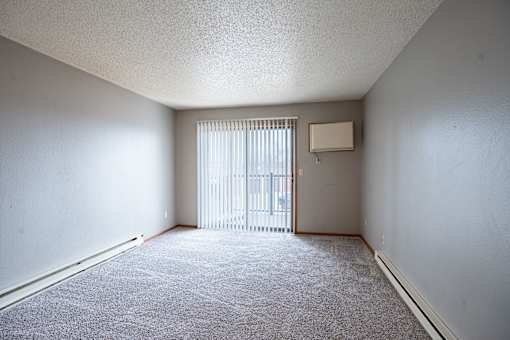 A room with a carpeted floor and a window with blinds. Fargo, ND Southgate Apartments