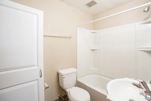 A white toilet sits next to a white sink in a small bathroom. Fargo, ND Birchwood Apartments
