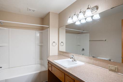 A bathroom with a sink, mirror, and tub. Fargo, ND L&R Apartments