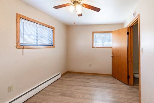 A room with a ceiling fan and two windows. Fargo, ND Birchwood Apartments