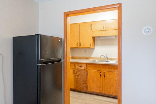 A black refrigerator is in a kitchen with wooden cabinets. Fargo, ND Birchwood Apartments