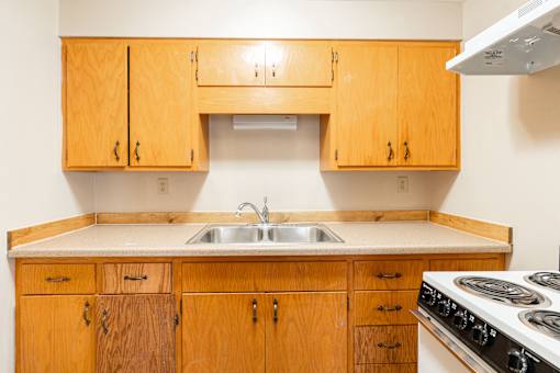 A kitchen with wooden cabinets and a white stove top oven. Fargo, ND Birchwood Apartments