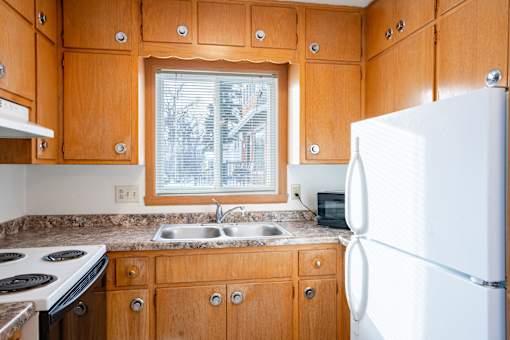 A kitchen with wooden cabinets and a white refrigerator. Fargo, ND L&R Apartments