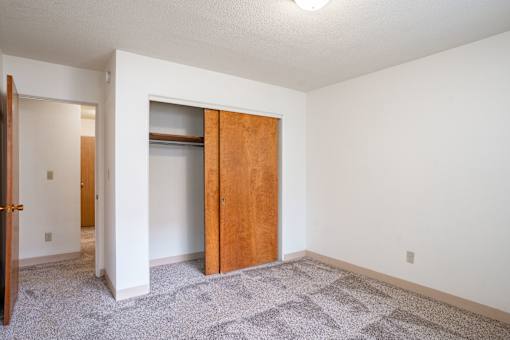 A room with a carpeted floor and a wooden door. Fargo, ND Islander Apartments