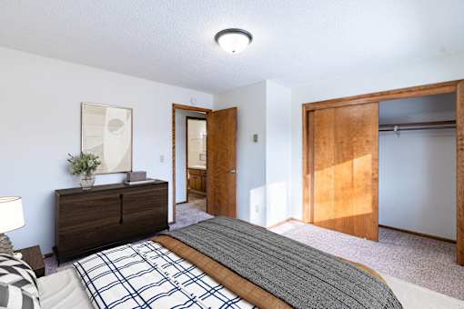 A bedroom with a bed, nightstand, and a painting on the wall. Fargo, ND Carr Apartments