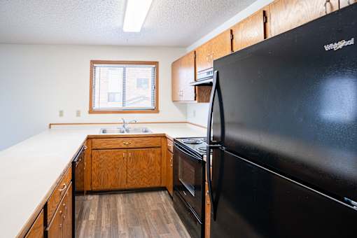 A black refrigerator is in the corner of a kitchen with wooden cabinets. Fargo, ND Westwood Estates