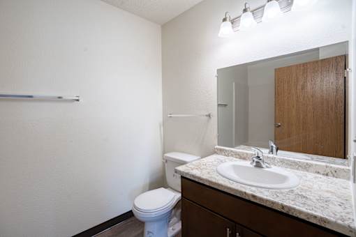 A white toilet sits in a bathroom next to a sink. Moorhead, MN Woodstone Apartments