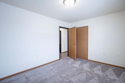 A room with a carpet and a wooden door. Moorhead, MN Woodstone Apartments