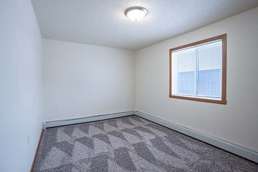 A room with a window and a carpeted floor. Moorhead, MN Woodstone Apartments