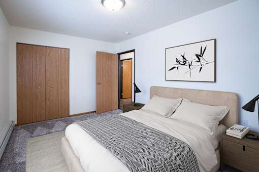 A bedroom with a bed, nightstand, and two doors. Moorhead, MN Woodstone Apartments
