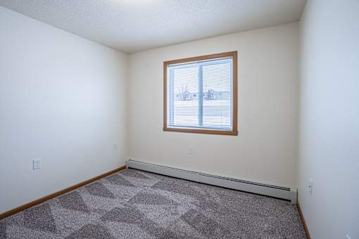 A room with a window and a carpet on the floor. Moorhead, MN Woodstone Apartments
