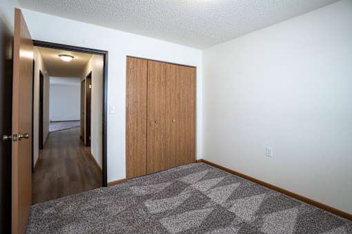 A hallway with a carpeted floor and a wooden door. Moorhead, MN Woodstone Apartments