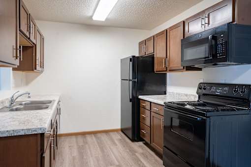 A kitchen with a black refrigerator, stove, and microwave. Moorhead, MN Woodstone Apartments