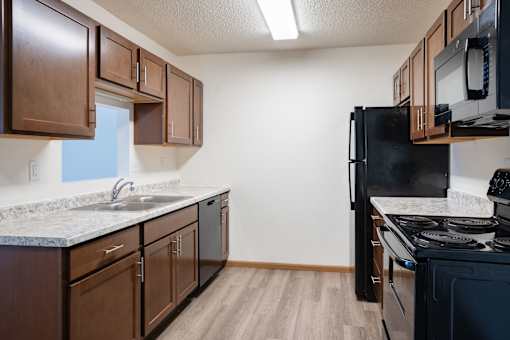 A kitchen with brown cabinets and a black refrigerator. Moorhead, MN Woodstone Apartments