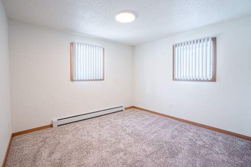 A room with a carpeted floor and two windows.