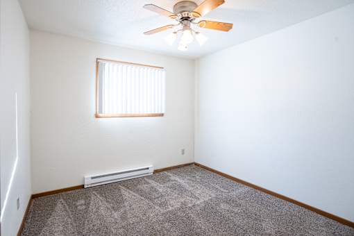 A room with a ceiling fan and a window with blinds. Fargo, ND Kennedy Apartments