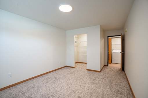 A room with a carpeted floor and a doorway leading to another room. Cherry Creek Apartments