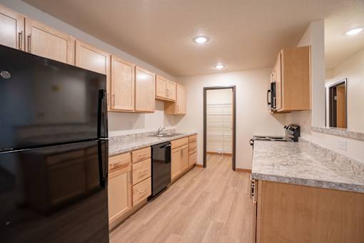 A kitchen with wood cabinets and black appliances. Cherry Creek Apartments