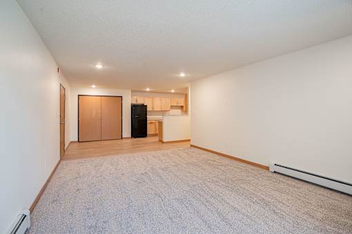 A spacious room with a carpeted floor and a door on the left. Cherry Creek Apartments