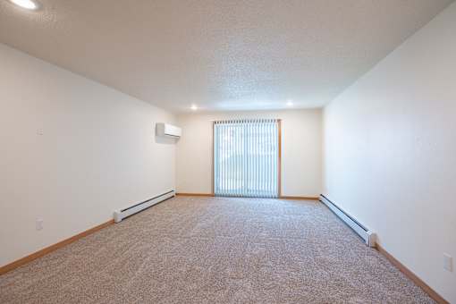 A spacious room with a carpeted floor and a window with blinds. Cherry Creek Apartments