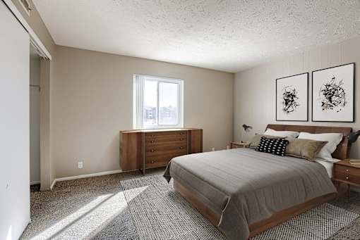 A bedroom with a bed, nightstand, and two framed pictures on the wall. Omaha, NE Evergreen Terrace Apartments